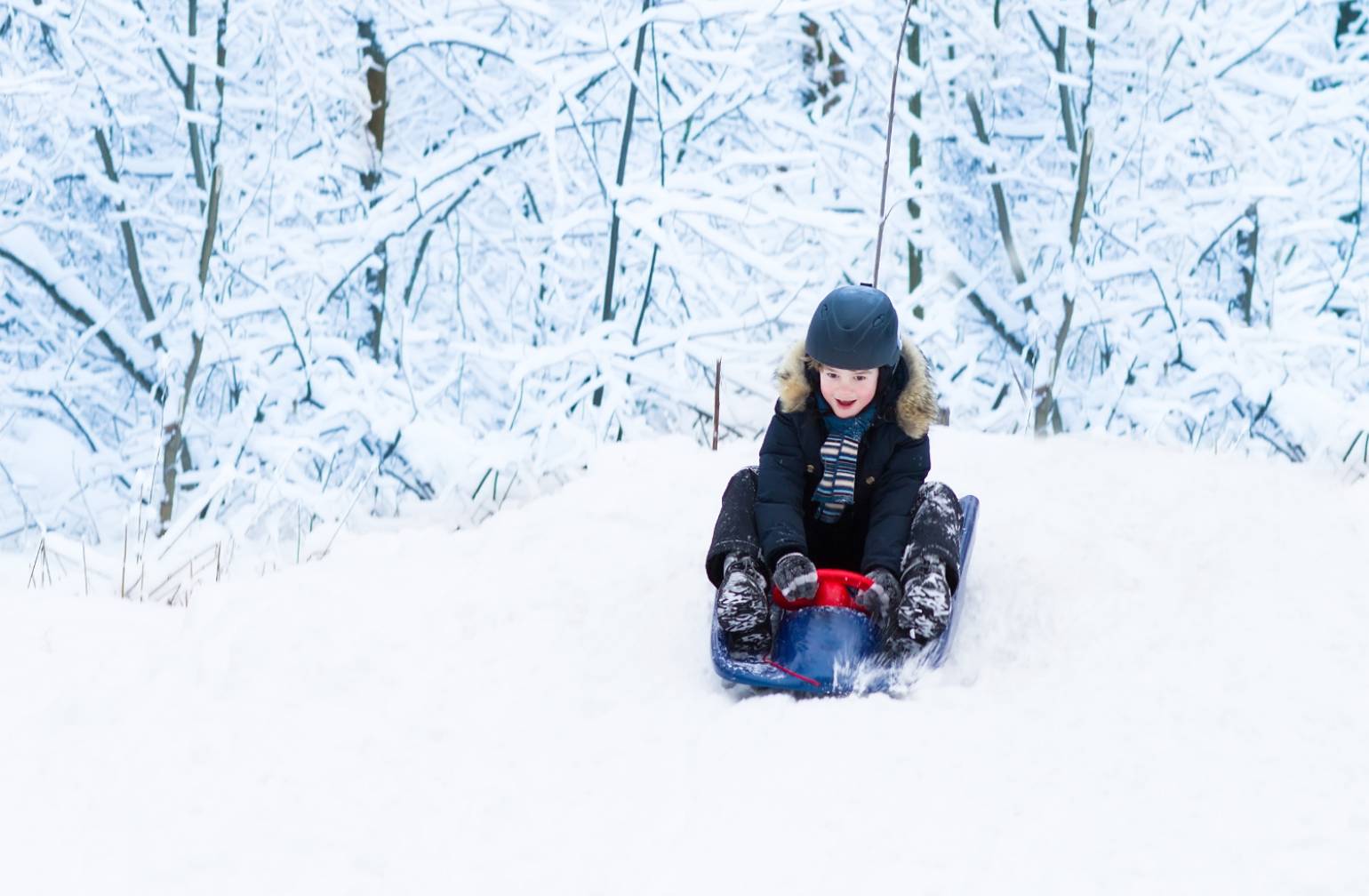 Boy sledding in the snow during winter.